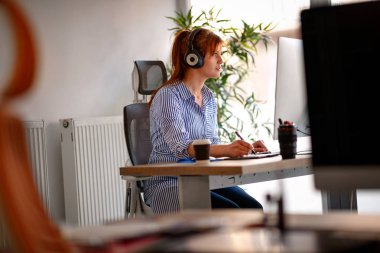 Genç kadın ofiste bir bilgisayarda çalışırken müzik