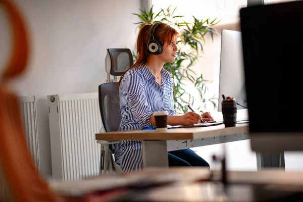Genç kadın ofiste bir bilgisayarda çalışırken müzik