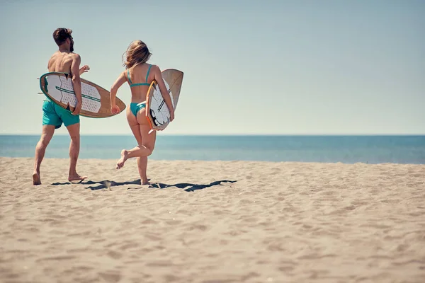 若い幸せな男と行く女性サーファーは 一緒にビーチでサーフィンをする — ストック写真