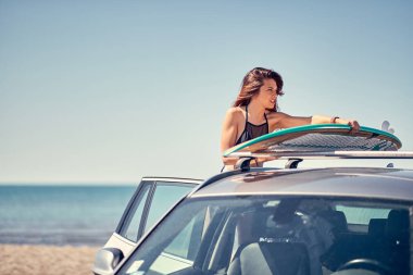 Yaz tatil yol gezisi tatil-genç gülümseyen sörfçü kız araba tatil onun surfboard ile plajda. Aşırı spor