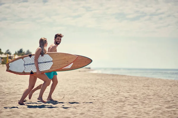若い幸せカップル一緒に行くサーファー ビーチでサーフィンをする — ストック写真