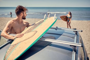 Gülümseyen genç sörfçü adam plajda sörf için hazırlanıyor