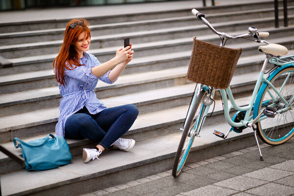 Молодая женщина фотографирует сидя на лестнице в городе
