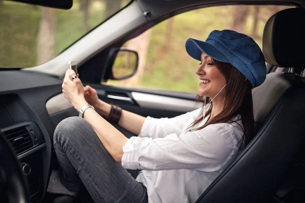 愉快的年轻妇女在耳机与智能手机听音乐在车里 — 图库照片