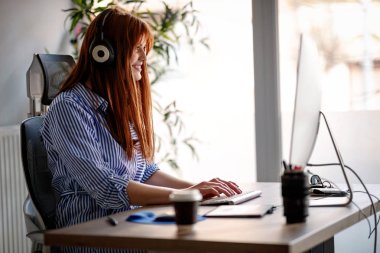 Kulaklıklar ile ofiste çalışan genç kadın tasarımcı