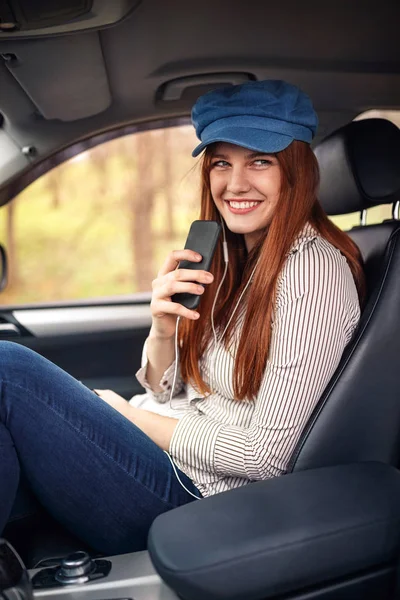 愉快的年轻女孩在耳机与智能手机听音乐在汽车 — 图库照片