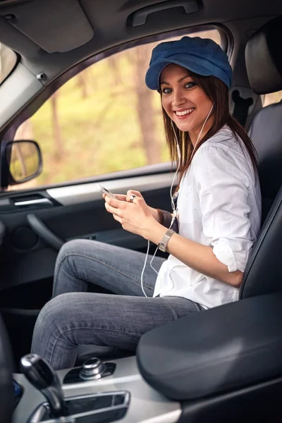 微笑的女孩听音乐与耳机移动在车里 — 图库照片