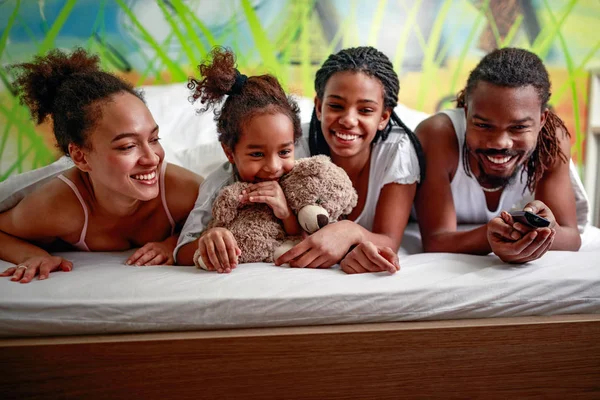 Smiling young African American family watching TV together in bedroom