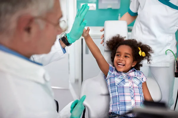 男性歯科医と冗談を作る歯科椅子に黒の陽気な若い女の子 — ストック写真