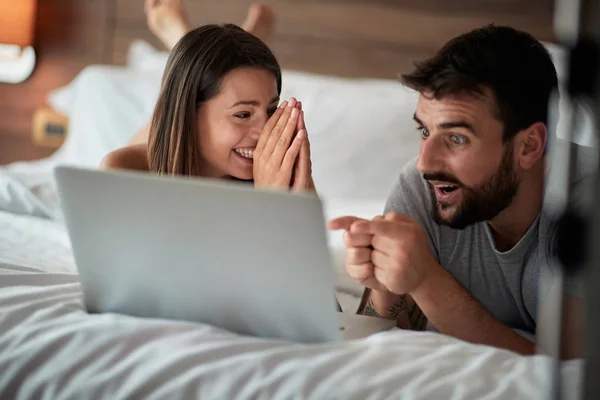 陽気なカップルが自宅のベッドに横になっているラップトップを使用して — ストック写真