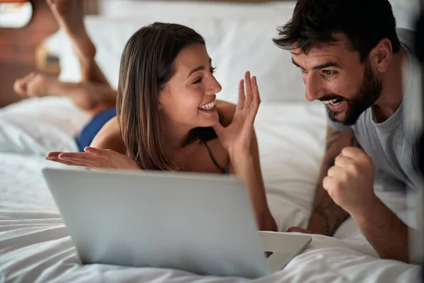 ベッド ベッドでノート パソコンを持つ幸せな若いカップルで面白い — ストック写真