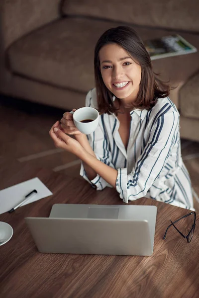 若いラップトップ コンピューターと家でリラックスした女の子を笑顔とコーヒー飲んで — ストック写真