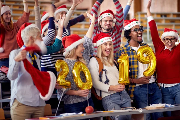 Happy Students in Santa hat holding 2019 golden balloons at New Year party on university