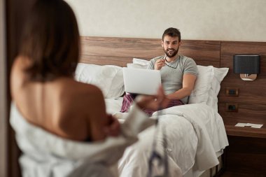 Seksi kadın yatakta dizüstü bilgisayarda çalışan genç adam ayartmaya