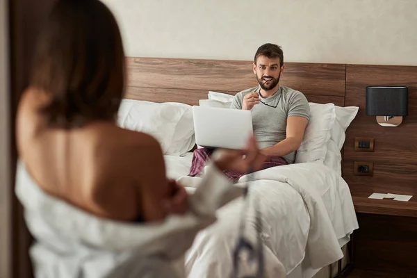 セクシーな女性のベッドでのラップトップに取り組んでいる若い男を誘惑しようとしています — ストック写真