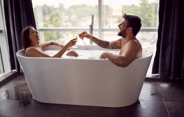 Genç erkek ve kız gülümseyerek küvette birlikte eğlenin ve şampanya içmek