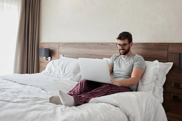 Souriant Jeune Homme Travaille Avec Ordinateur Portable Couché Sur Lit — Photo