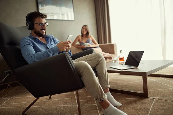 Hombre utiliza un teléfono con auriculares para escuchar música y relajarse en casa —  Fotos de Stock