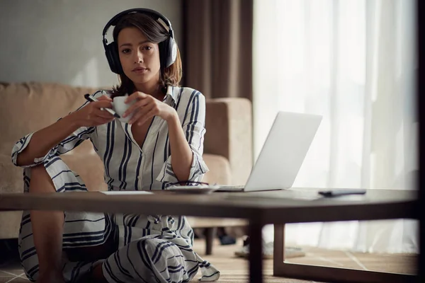 Chica utiliza un ordenador portátil con auriculares para escuchar música y relajarse —  Fotos de Stock