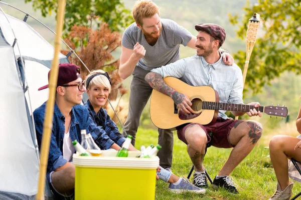 Tatuado chico tocar la guitarra y sonreír con amigos —  Fotos de Stock