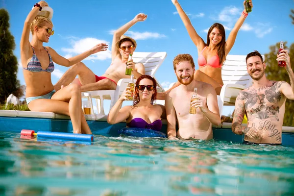 Amigos posando com garrafas de bebida na piscina — Fotografia de Stock