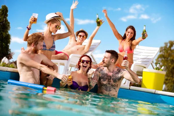 Happy boys and girls spend free time at pool with drinks — Stock Photo, Image