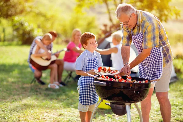 Smiling grandfather giving grandson grilling meal — Stock Photo, Image