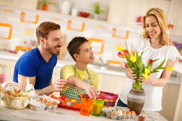 Father with son coloring eggs while mother arranges tulips in vase — Stock Photo, Image