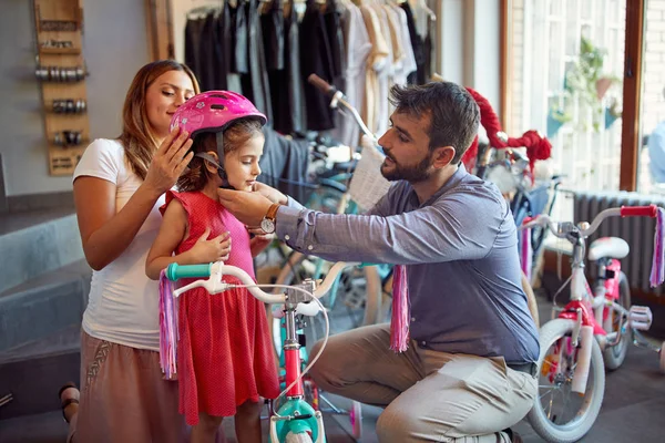 Pai e mãe compras nova bicicleta e capacetes para pequeno gi — Fotografia de Stock