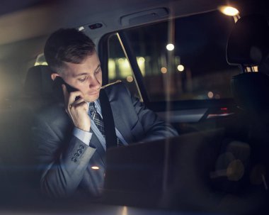otomobilin arka koltuğunda telefonda konuşurken dizüstü bilgisayar üzerinde çalışan işadamı