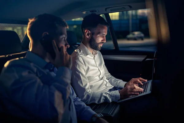 Trabajar en el ordenador portátil en el asiento trasero del coche por la noche —  Fotos de Stock