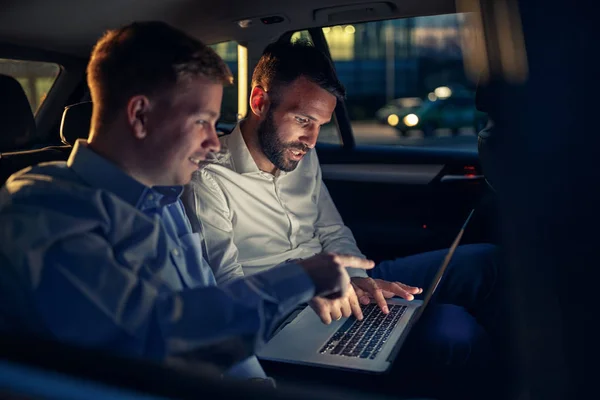 Empresarios en coche trabajando en el ordenador portátil en el asiento trasero —  Fotos de Stock