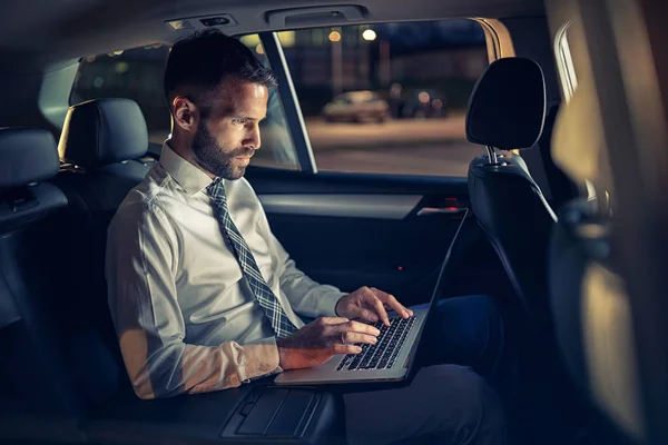 Hombre de negocios serio trabajando hasta tarde en el coche en el ordenador portátil —  Fotos de Stock