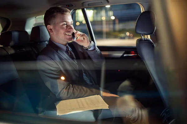 Sonriente hombre de negocios moderno trabajando hasta tarde en el coche — Foto de Stock