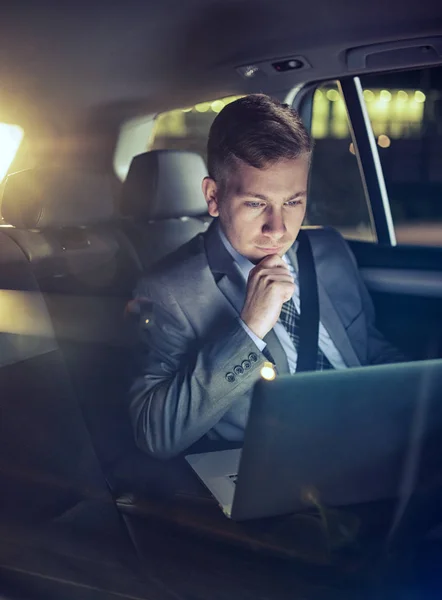 Σοβαρός επιχειρηματίας στη μετακίνηση του αυτοκινήτου ελέγχοντας την εργασία του σε φορητό υπολογιστή — Φωτογραφία Αρχείου