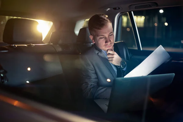 Centrándose en el trabajo- hombre de negocios trabajando en su computadora portátil y papel en el asiento trasero del coche —  Fotos de Stock