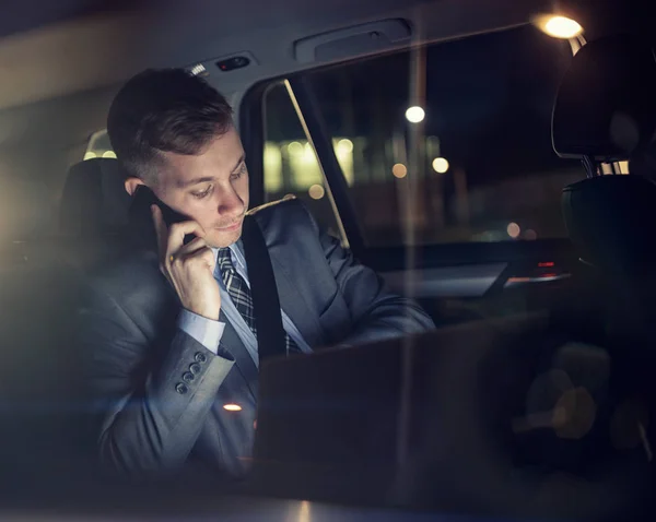 Homem de negócios trabalhando em seu laptop falando no telefone no banco de trás do carro — Fotografia de Stock