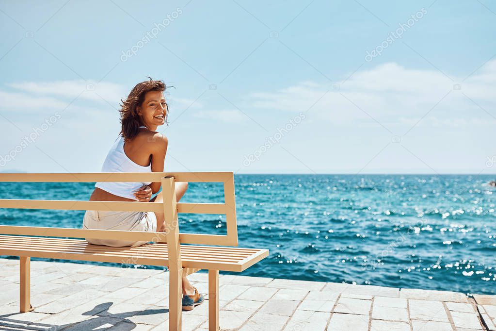 Beautiful girl traveler sitting on bench near the beach 