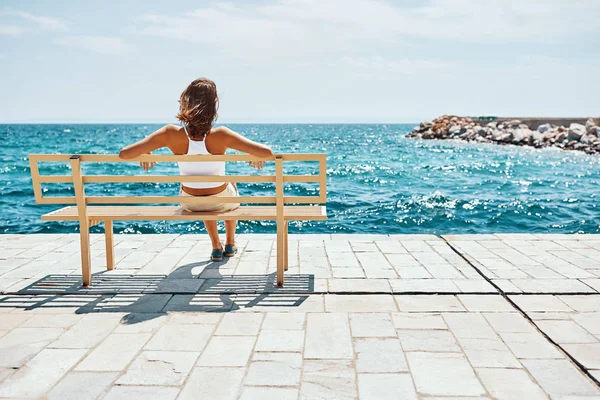 Vrouw kijken naar de zee zitten op een bank — Stockfoto