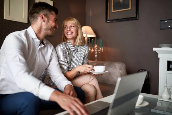 Glada partners dricker kaffe och jobbar på laptop — Stockfoto