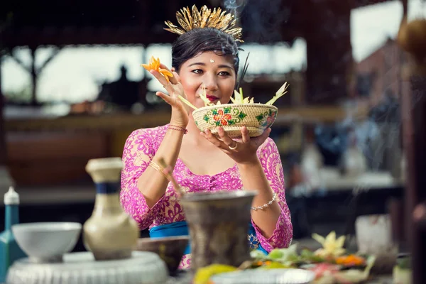 Balinese woman in a pink dress making flower offerings to the God — Stock Photo, Image