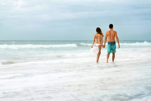 Pareja joven caminando a través de olas — Foto de Stock