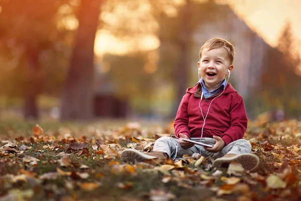 Niño escuchar música en el teléfono inteligente en el parque de otoño —  Fotos de Stock