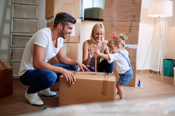 Happy parents with child moving in new home unpacking boxes — Stock Photo, Image