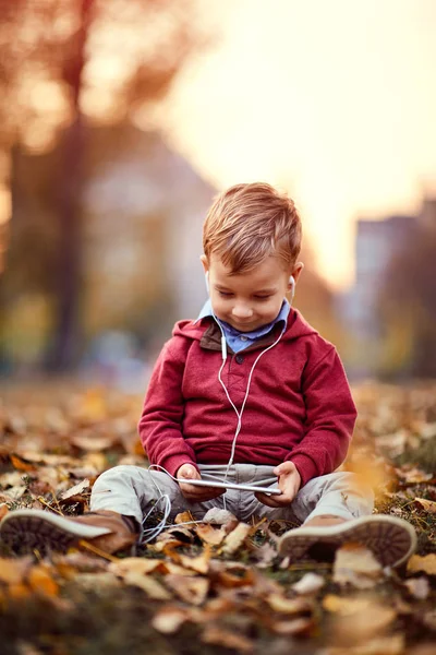Szczęśliwy chłopiec słuchać muzyki na telefon komórkowy w parku — Zdjęcie stockowe
