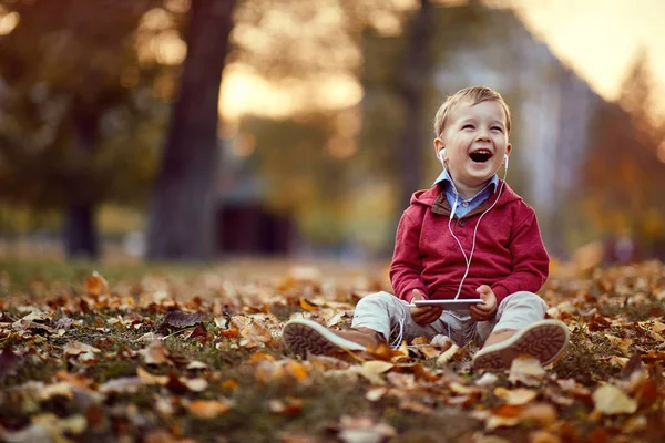 Ragazzo sorridente ascolta musica su smartphone. Famiglia, infanzia, stagione e concetto di persone — Foto Stock