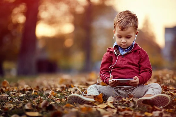 Niño escuchar música en el teléfono inteligente en el parque de otoño — Foto de Stock