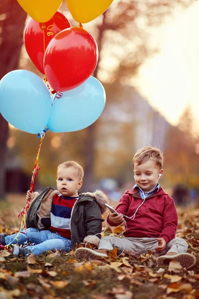 Hermanos jugando con globos y teléfonos inteligentes en el parque de otoño — Foto de Stock