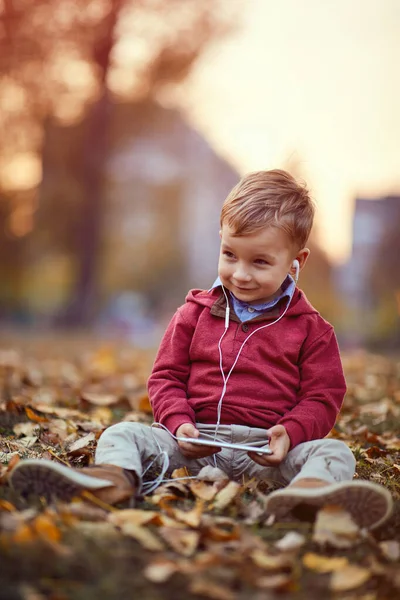 Niño feliz escuchar música en el teléfono móvil en el parque — Foto de Stock