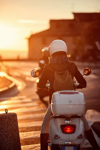 Reisen mit dem Motorroller. Mädchen fährt Motorroller auf Straße bei Sonnenuntergang. — Stockfoto